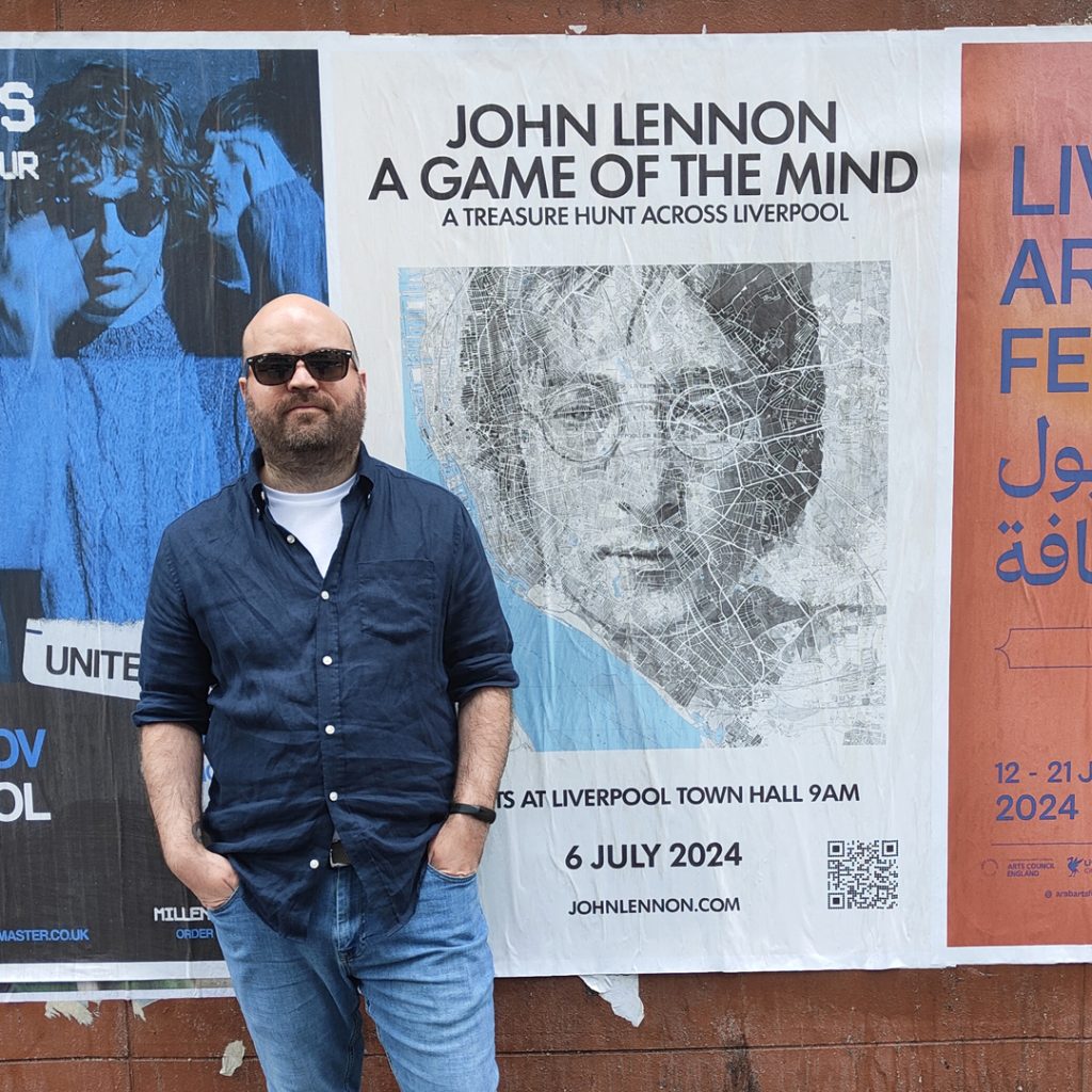 Ed Fairburn in front of John Lennon a game of the mind poster in Liverpool